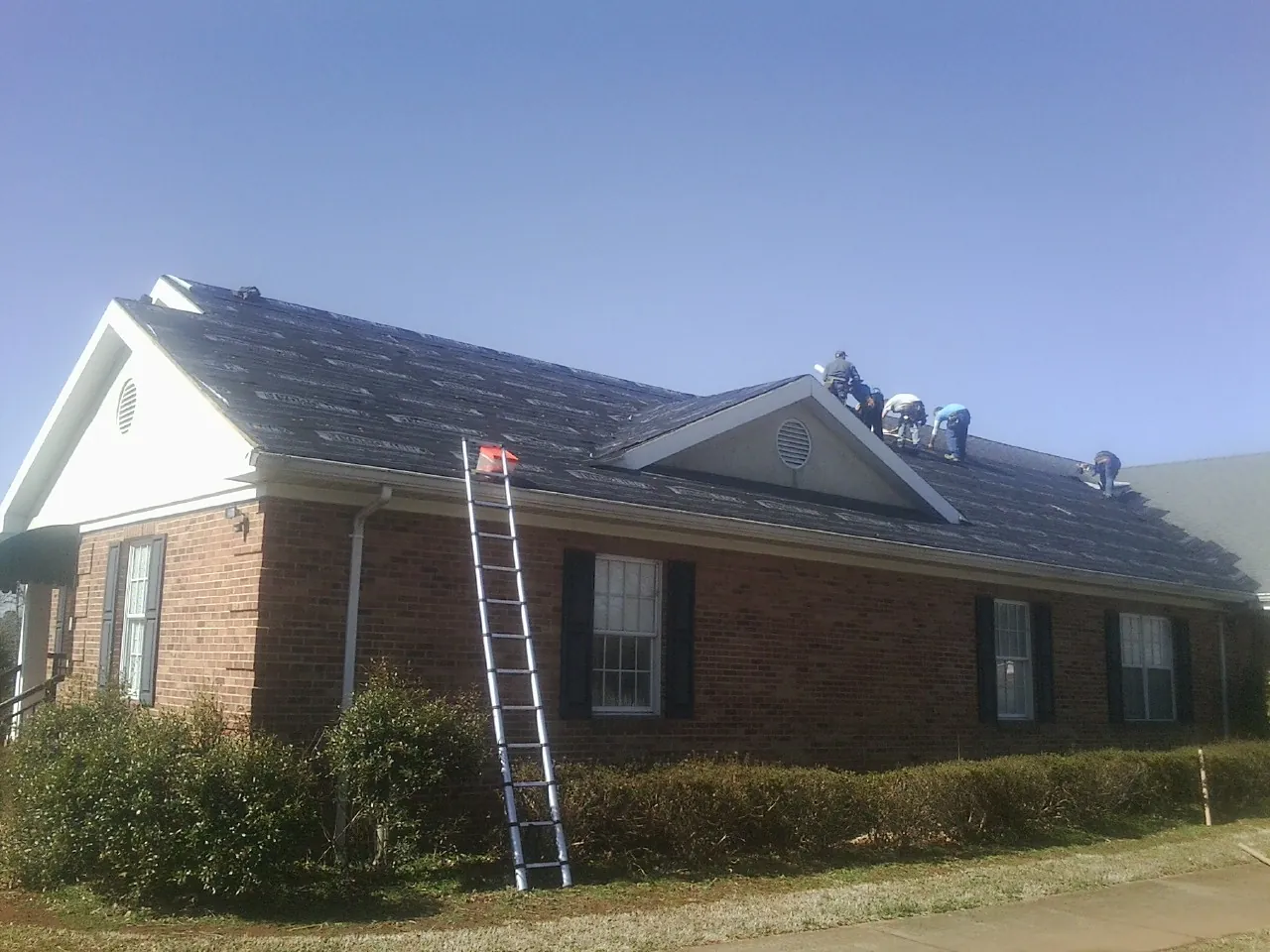 Crew tearing shingles off a brick ranch roof with a ladder set — Emergency Roof Repair work by our crew in North Weymouth