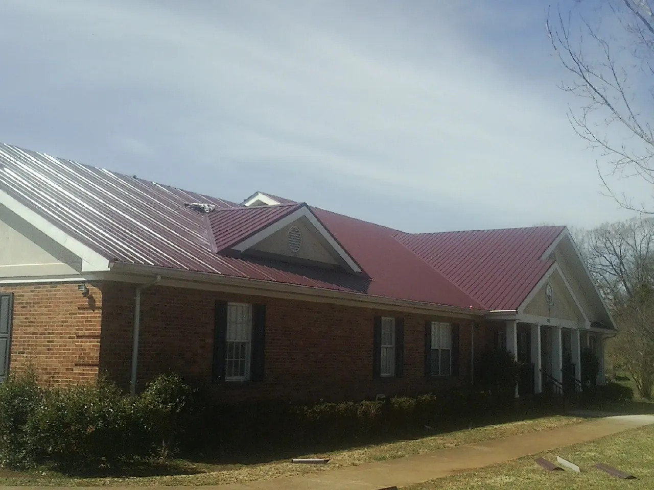 Red metal roof with gabled entries on a long brick building, from a Hail Damage Roof Repair job in North Weymouth