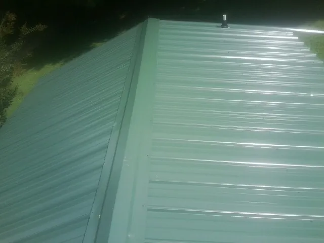 New green metal panels meeting at the ridge of a roof — Flat Roof Repair work by our crew in North Weymouth