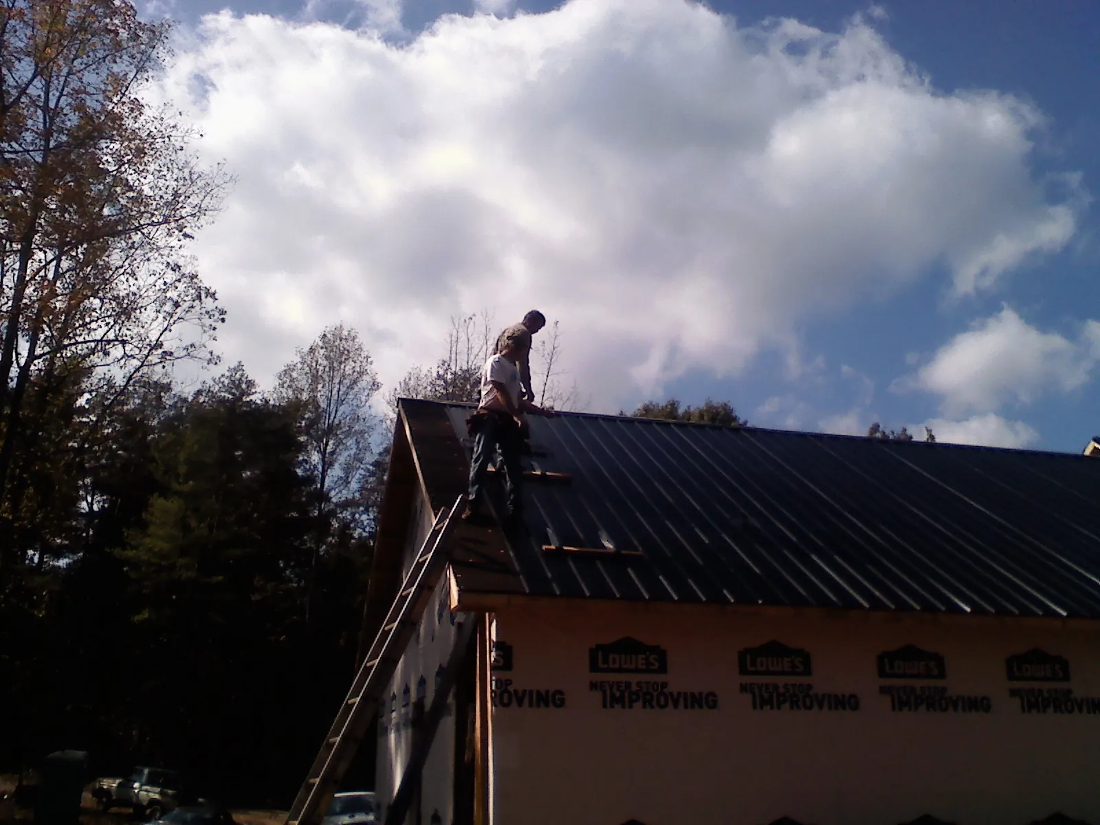 Roofer fastening dark metal panels high against a cloudy sky, from a Roof Inspection job in North Weymouth