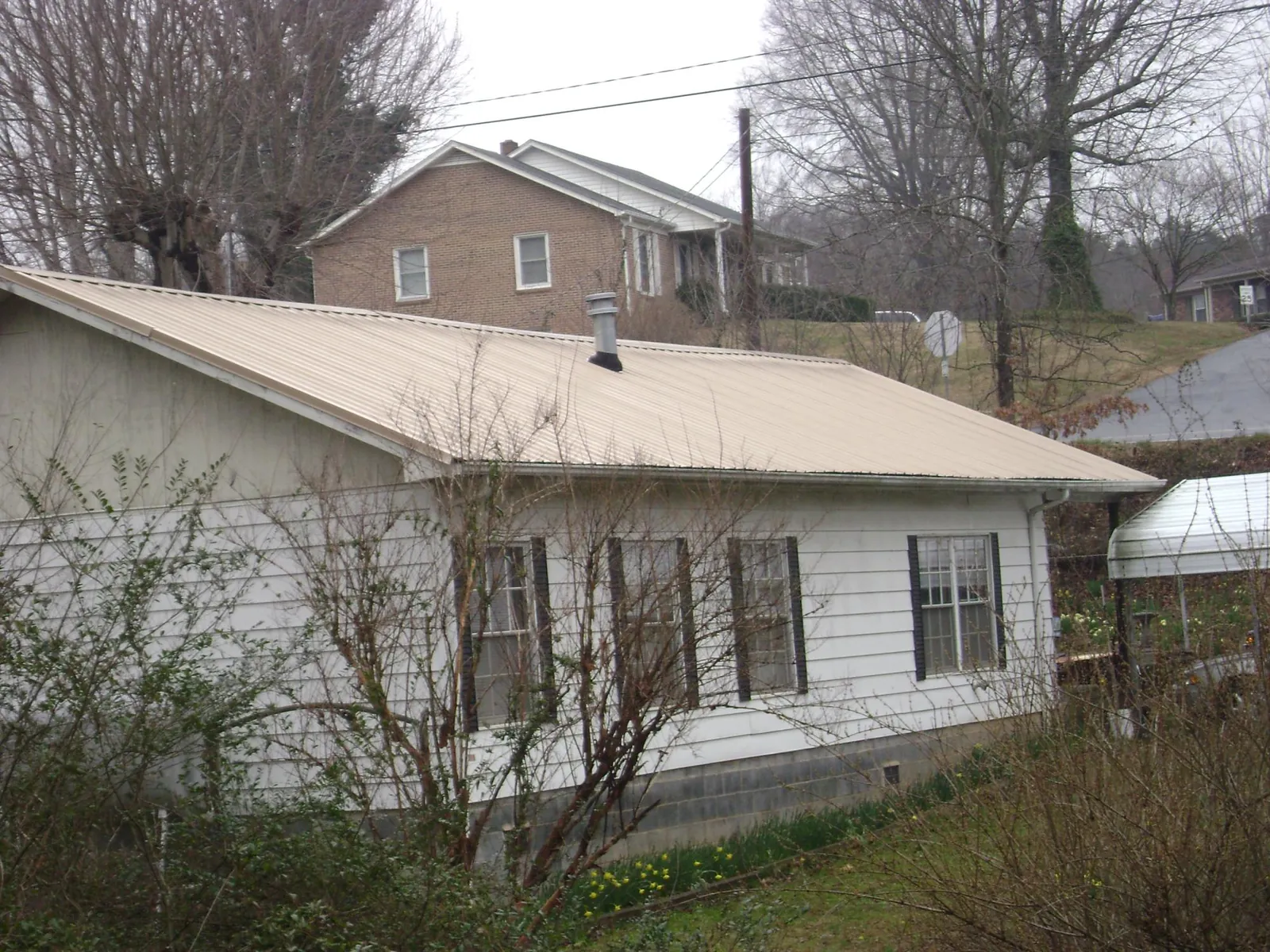 Tan metal roof on a white sided house set into a hillside — Commercial Roofing by Roofing Brothers in North Weymouth